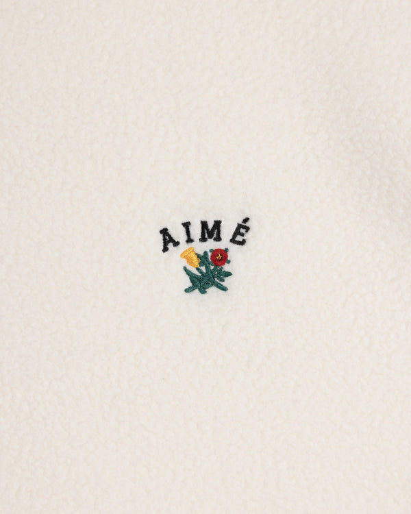 Crest Quarter-Zip Fleece Pullover with AIMÉ text and a small yellow and red flower embroidered on white fleece.