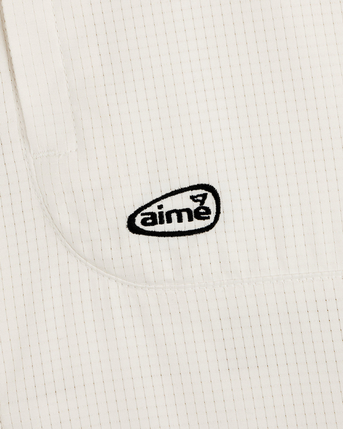 Close-up of the ALD Golf Lightweight Tips Windbreaker’s white, textured fabric with thin stripes and black aime logo.