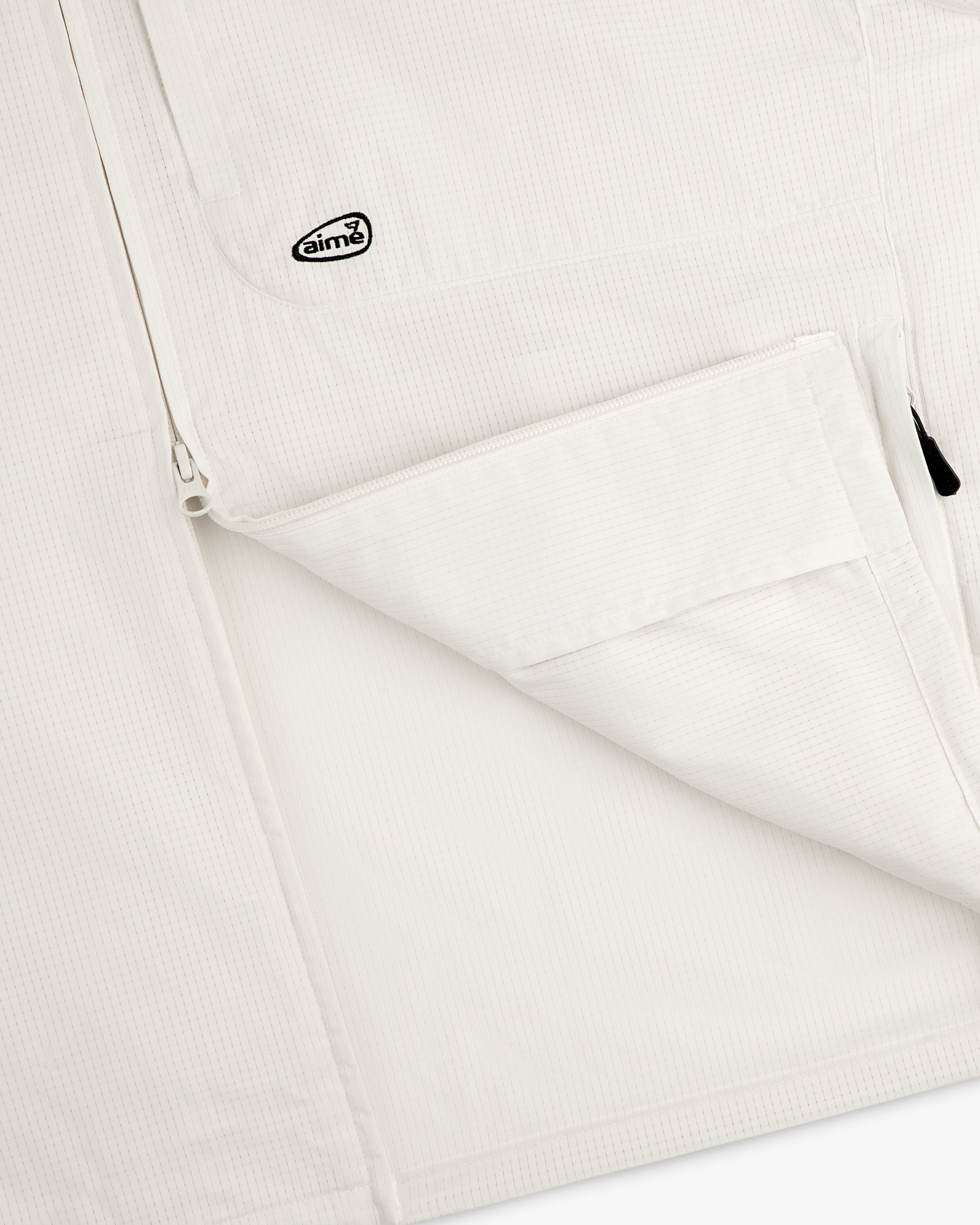 Close-up of the ALD Golf Lightweight Tips Windbreaker, featuring a zip pocket and small Aimé logo patch near the zipper.