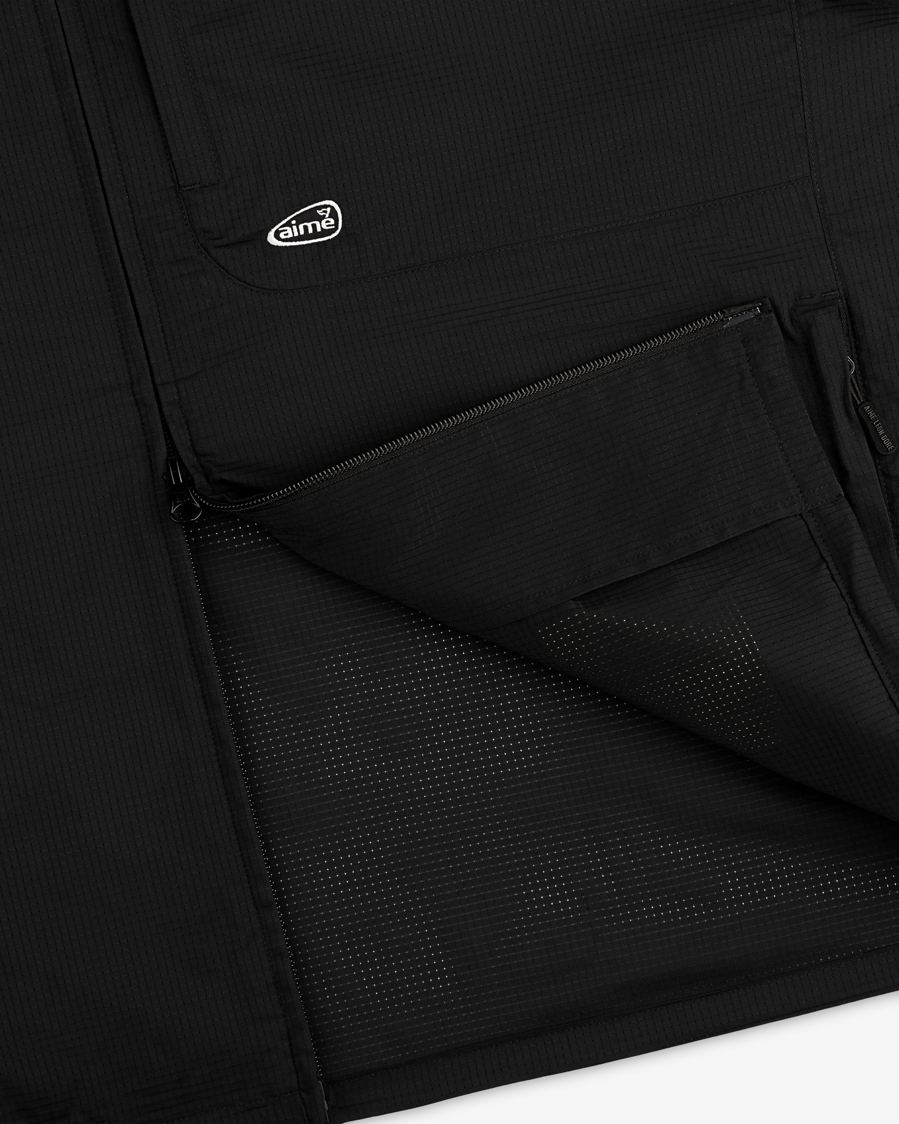 Close-up of the ALD Golf Lightweight Tips Windbreaker’s black pocket, half-zipped, with logo patch above.