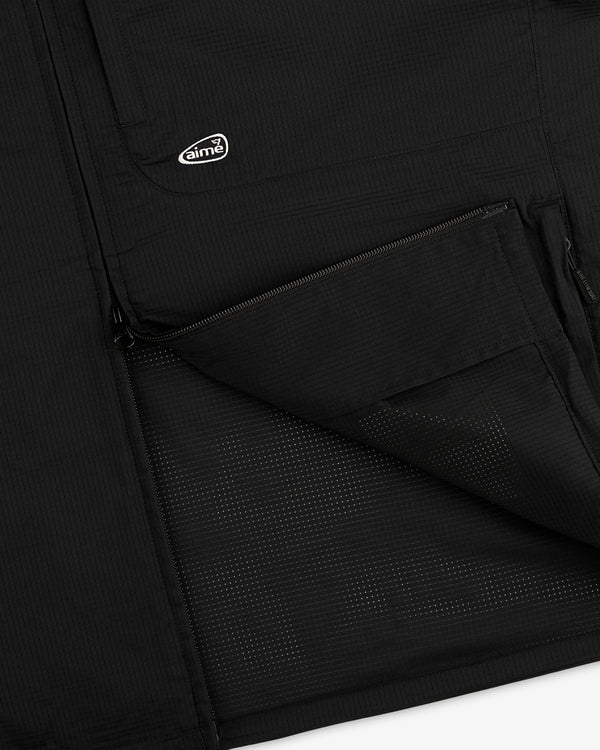 Close-up of the ALD Golf Lightweight Tips Windbreaker’s black pocket, half-zipped, with logo patch above.