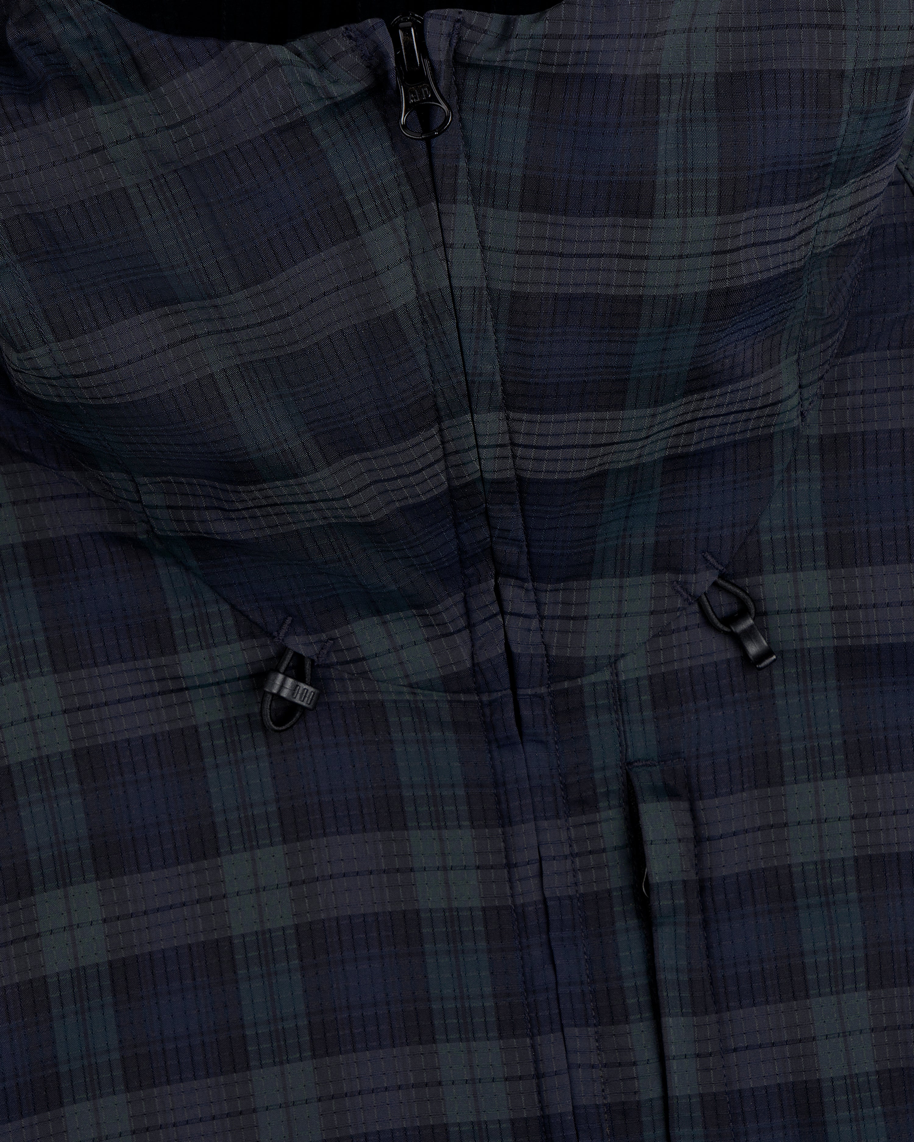 Close-up of the ALD Golf Lightweight Tips Windbreaker featuring a plaid pattern, zipper, and two black toggle adjusters.