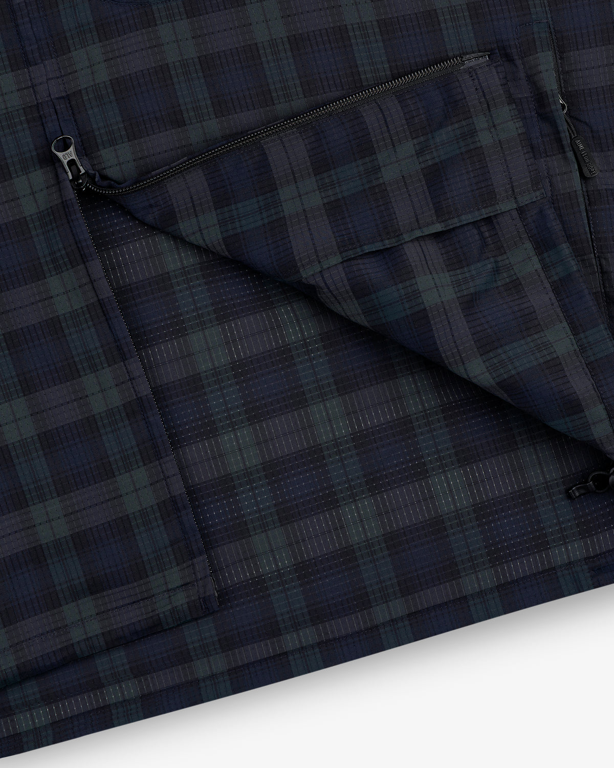 Close-up of the ALD Golf Lightweight Tips Windbreaker in navy and green plaid with a zippered pocket and visible stitching.