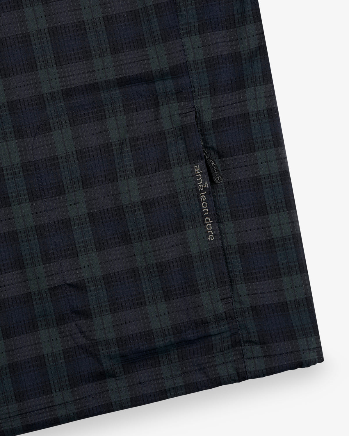 Close-up of ALD Golf Lightweight Tips Windbreaker in dark green and navy plaid with a small label near the seam.