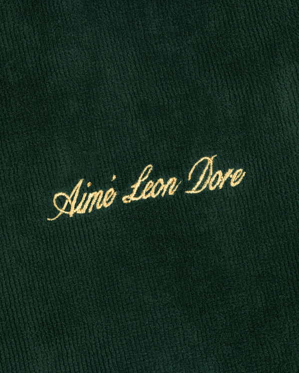 Gold script text Aimé Leon Dore embroidered on dark green ribbed Mulberry Robe fabric.
