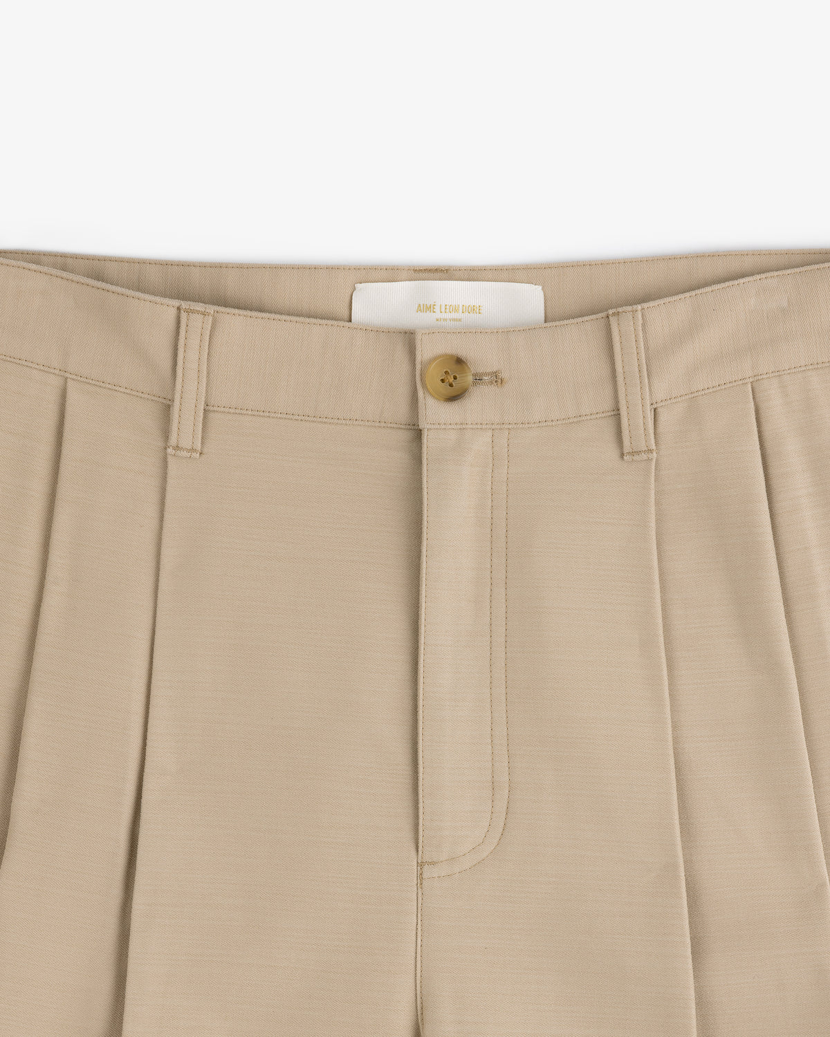 Close-up of Double Pleated Pant in beige with a brown button and belt loops at the waistband.