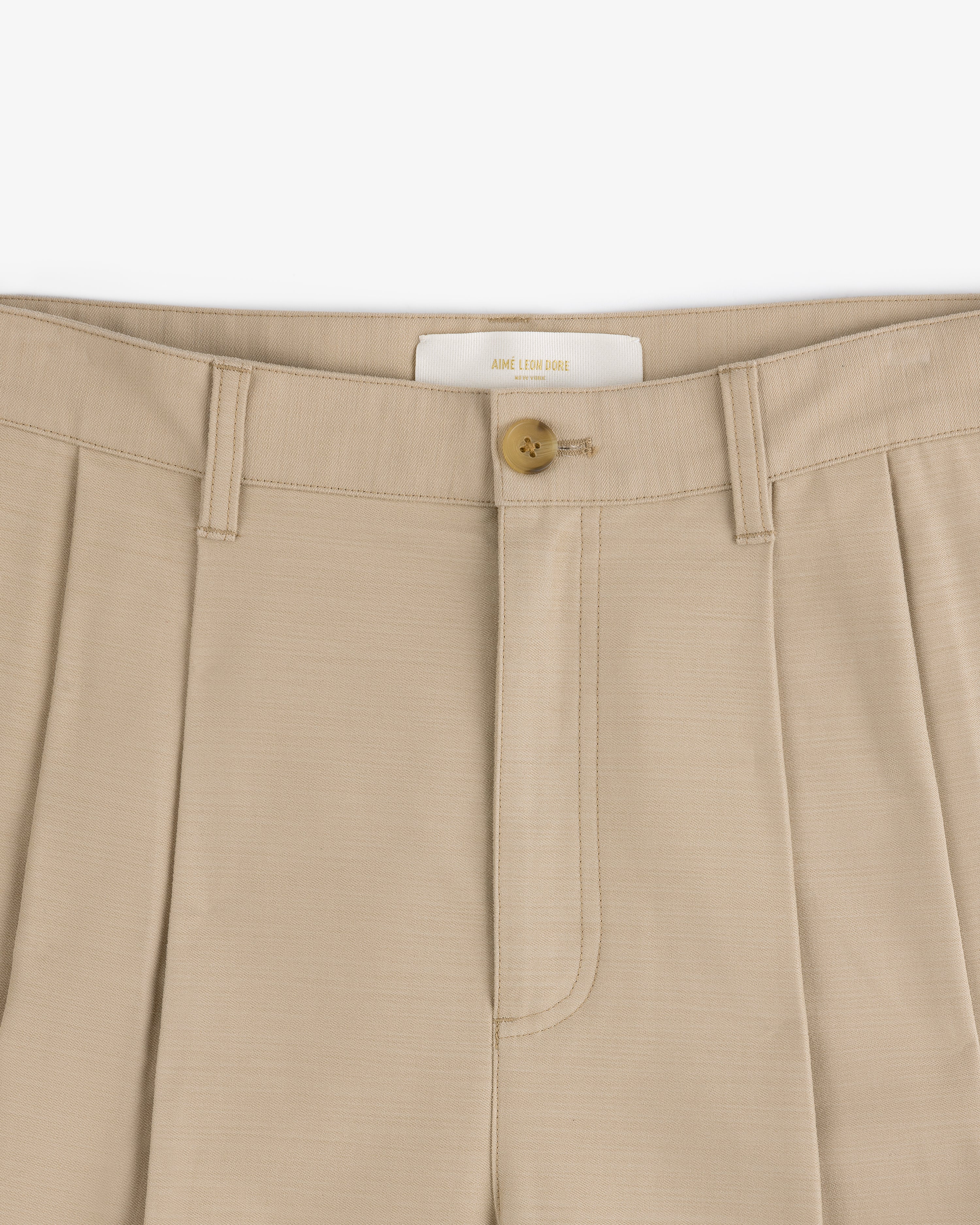 Close-up of Double Pleated Pant in beige with a brown button and belt loops at the waistband.