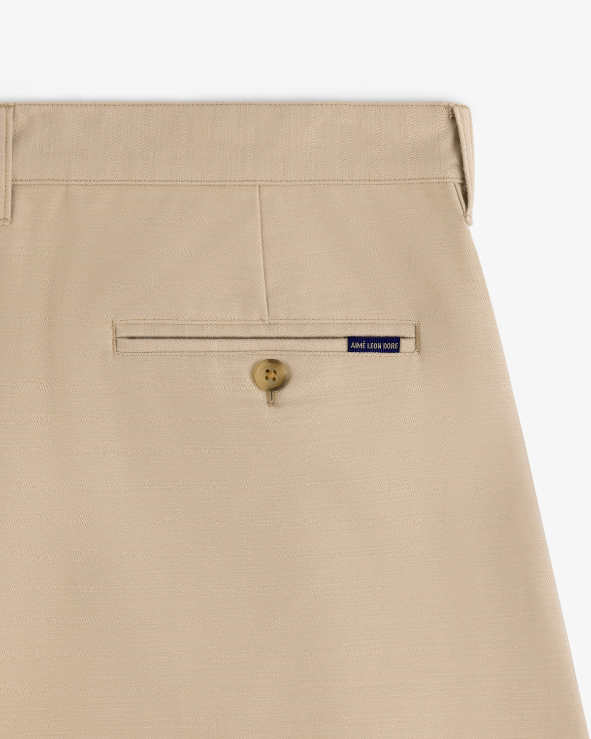 Close-up of the Double Pleated Pant in beige, featuring a buttoned back pocket and a small blue ALD label above it.
