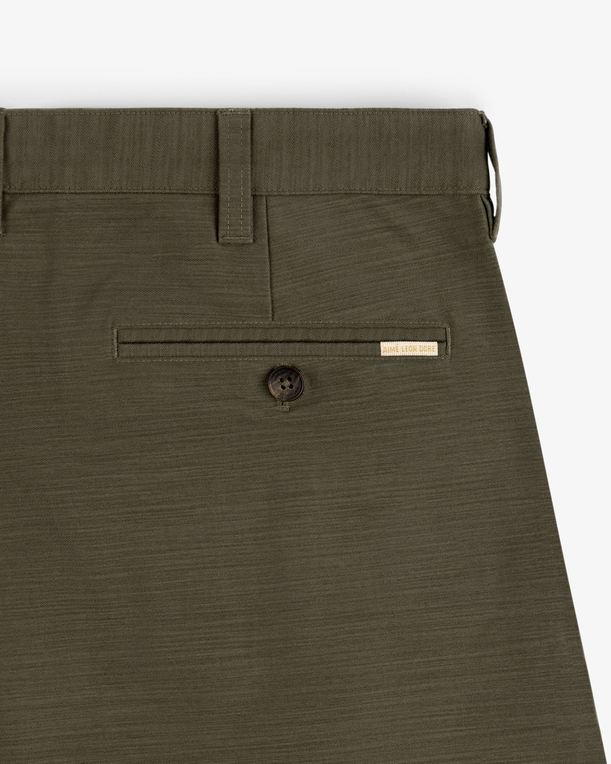 Close-up of Double Pleated Pant in olive green, highlighting the back pocket with button and WELL WORN CORES label.