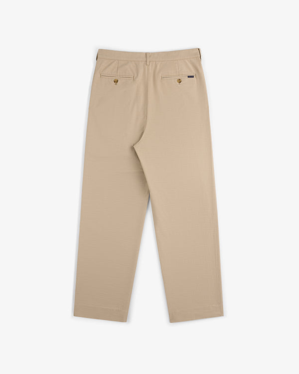 Double Pleated Pant in beige, shown from the back with two buttoned pockets and straight legs on a white background.
