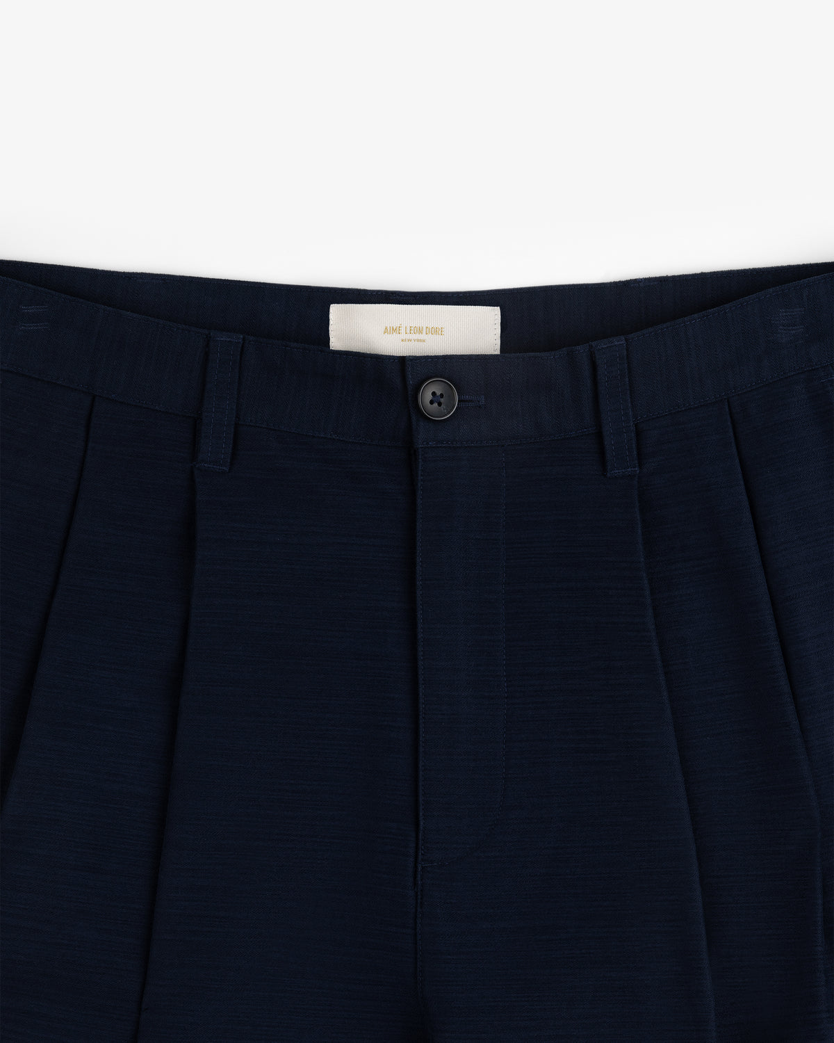 Double Pleated Pant: Navy blue dress pants with waistband, belt loops, pleats, and a black button above the zipper.