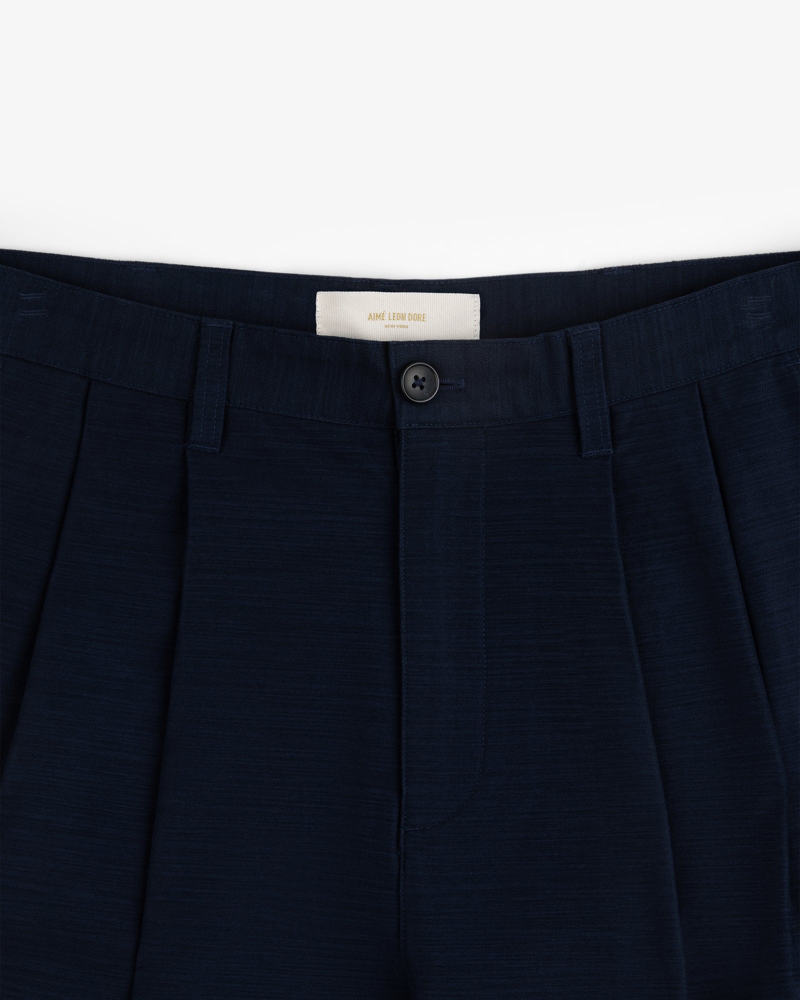 Double Pleated Pant: Navy blue dress pants with waistband, belt loops, pleats, and a black button above the zipper.
