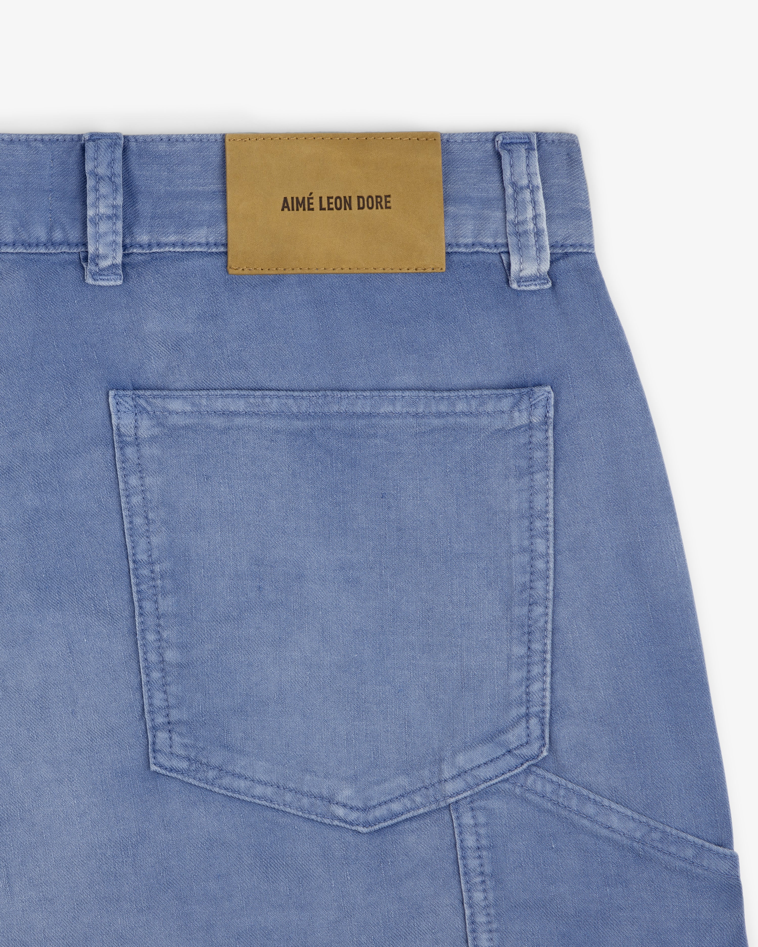 Close-up of light blue Linen Blend Carpenter Pant with back pocket and tan leather AIMÉ LEON DORE patch above it.
