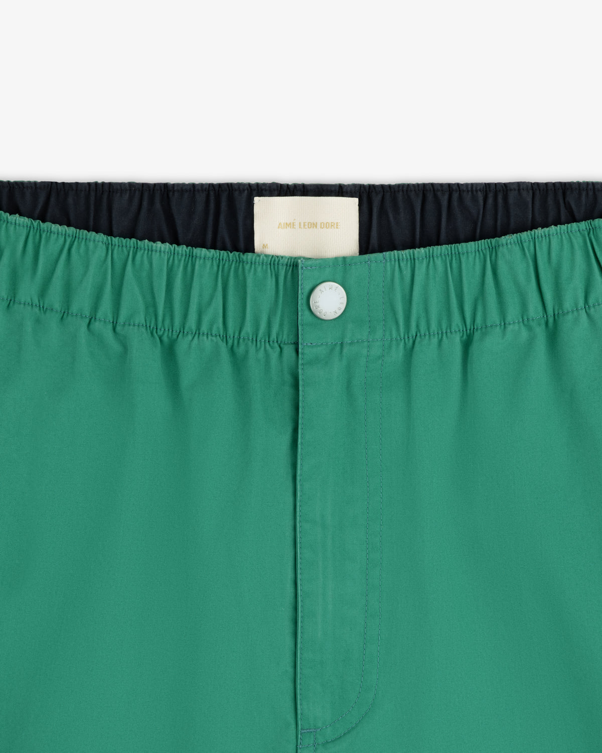 Close-up of Washed Cotton Windbreaker Pant in green, featuring an elastic waistband, front button, and white inner label.