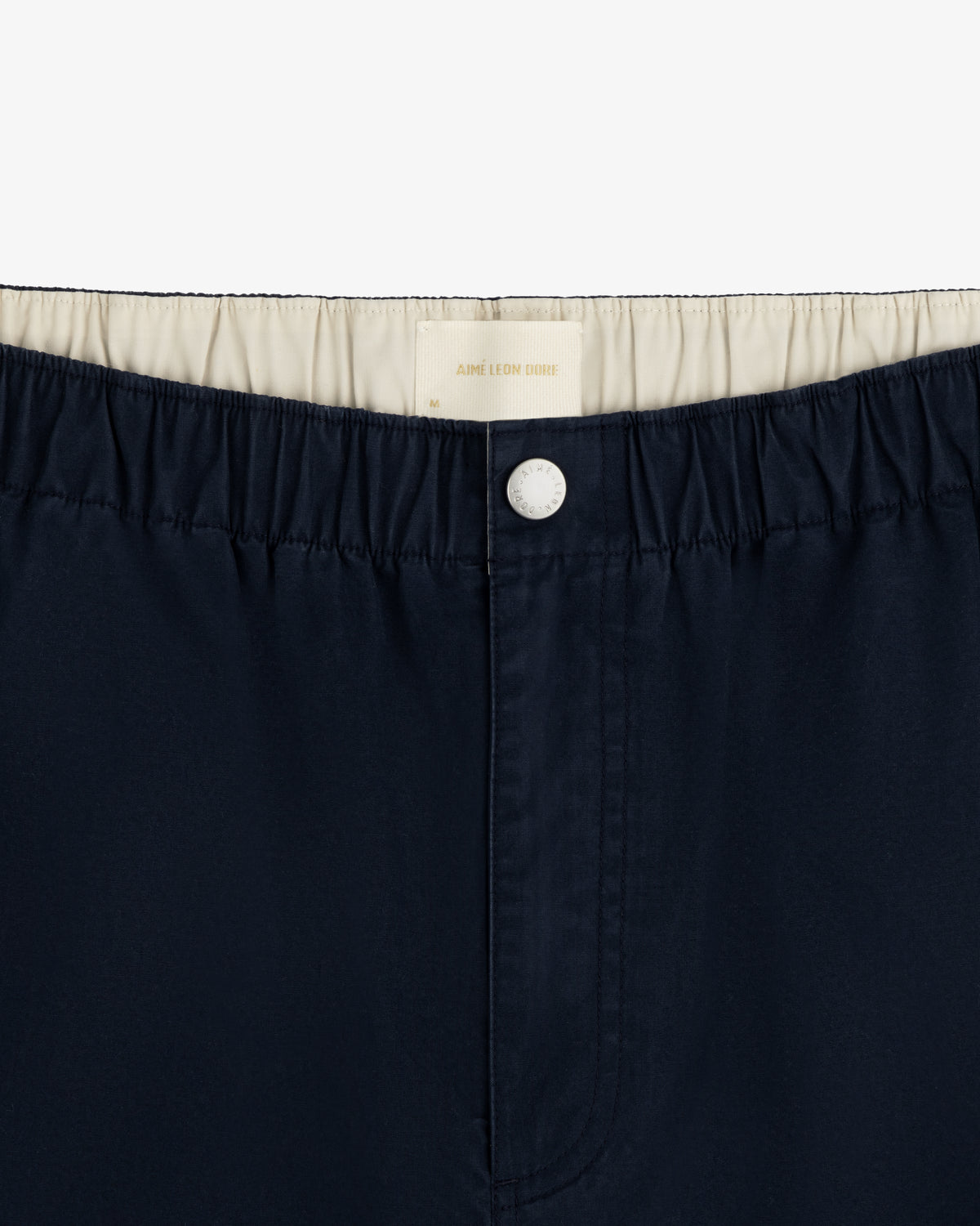 Washed Cotton Windbreaker Pant in navy blue with elastic waistband, white button, and cream lining.