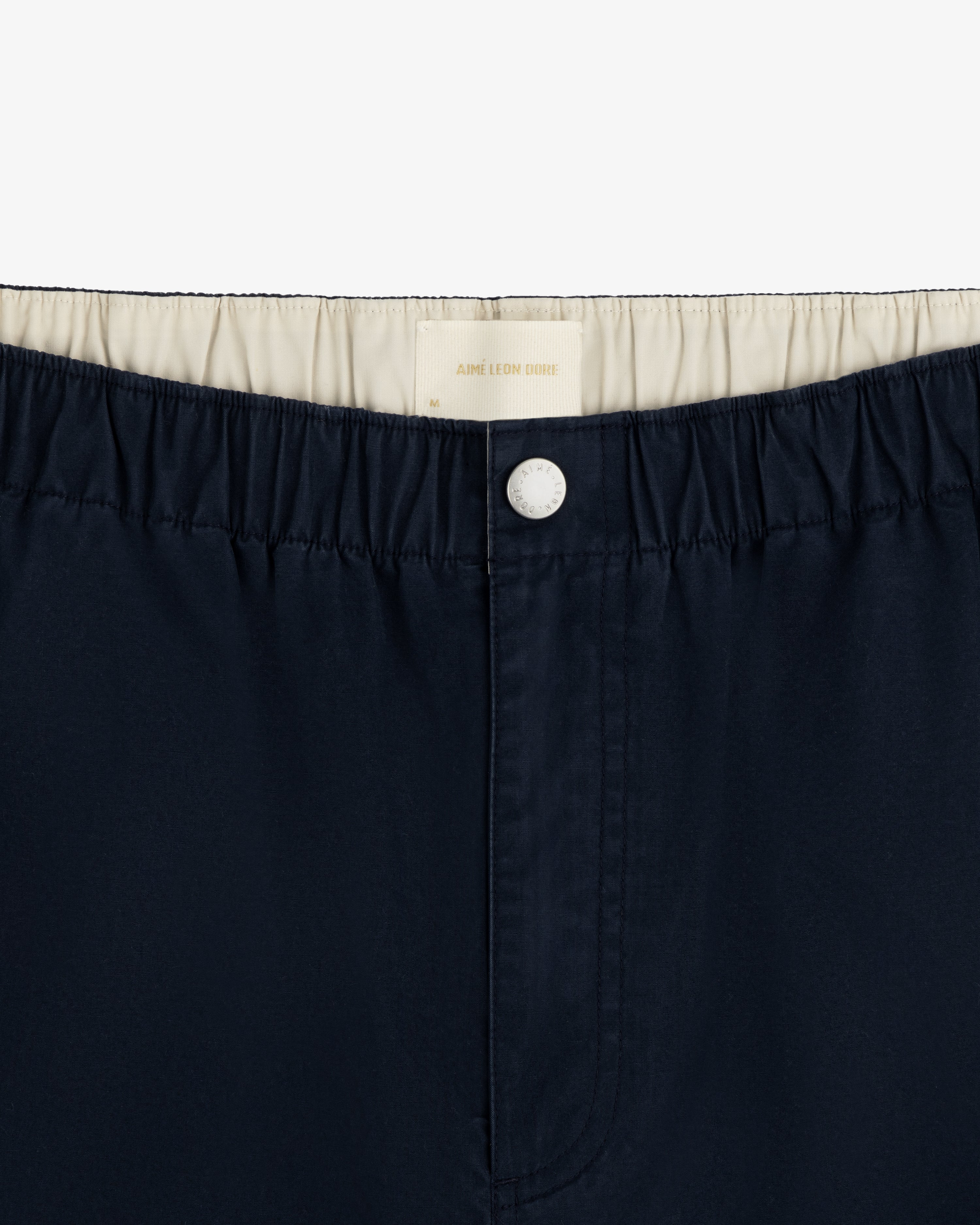 Washed Cotton Windbreaker Pant in navy blue with elastic waistband, white button, and cream lining.