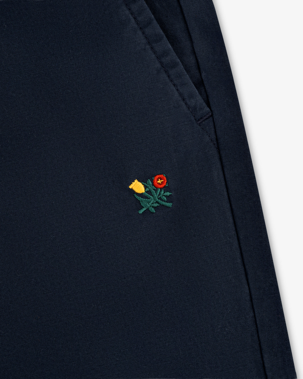 Close-up of the Washed Cotton Windbreaker Pant in navy blue with a small yellow and red flower near the pocket.