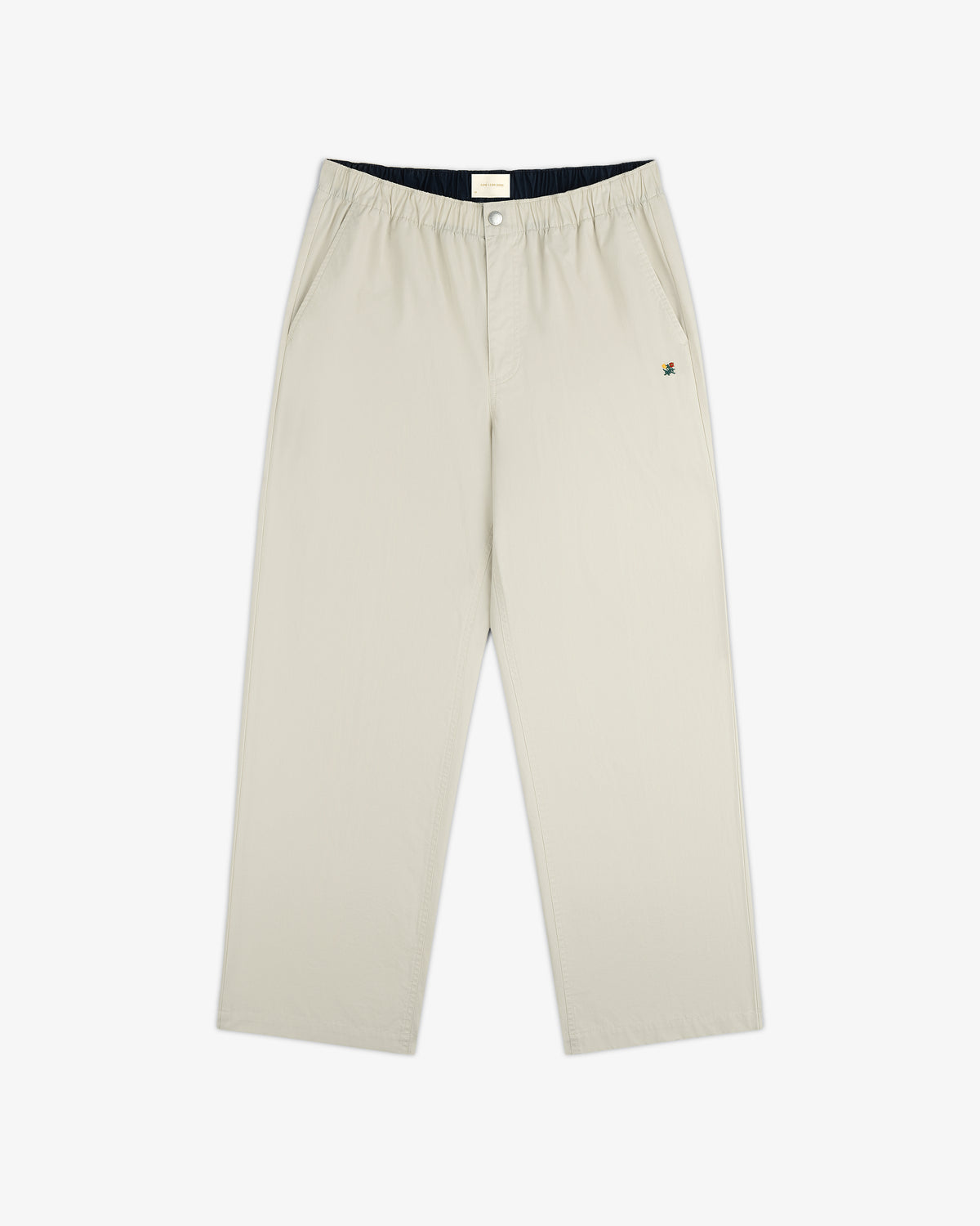 Washed Cotton Windbreaker Pant in beige with wide legs, side pockets, elastic waist, and a small logo near the left pocket.
