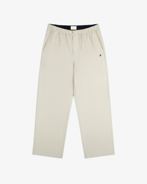 Washed Cotton Windbreaker Pant in beige with wide legs, side pockets, elastic waist, and a small logo near the left pocket.
