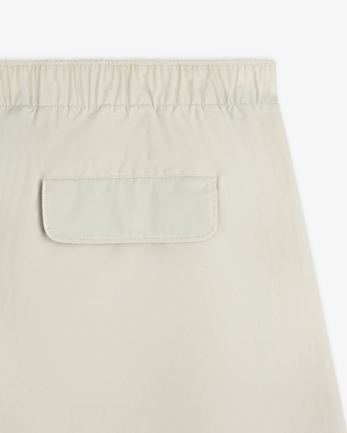 Close-up of the Washed Cotton Windbreaker Pant in beige, featuring an elastic waistband and a flap back pocket.