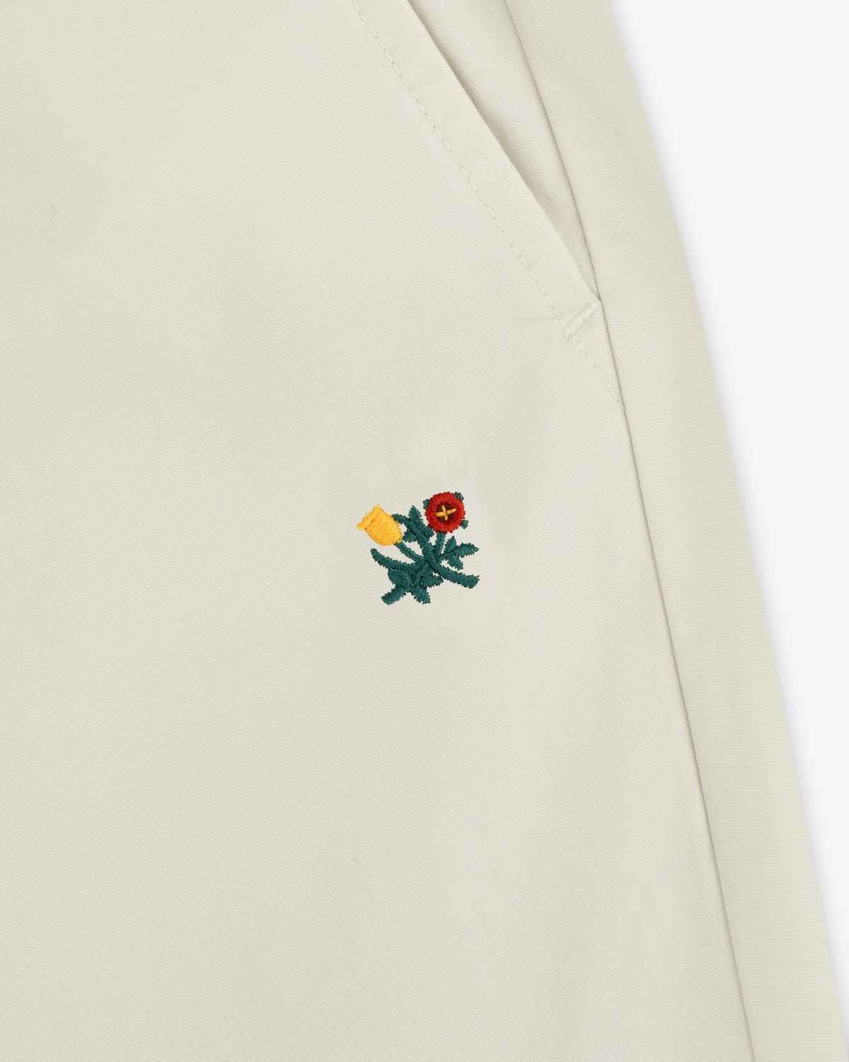 Close-up of a Washed Cotton Windbreaker Pant in cream with a small red and yellow embroidered flower near the seam.