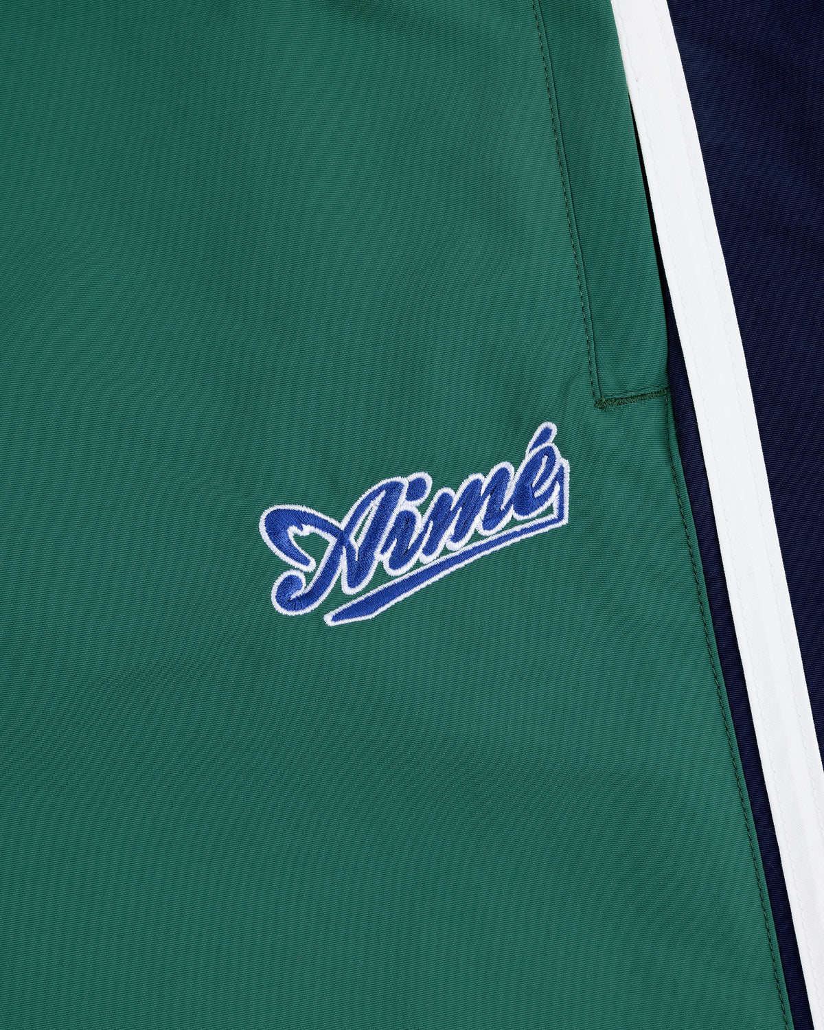 Green fabric with "Aimé" in blue/white cursive beside white and navy panels on the Colorblock Track Pant.