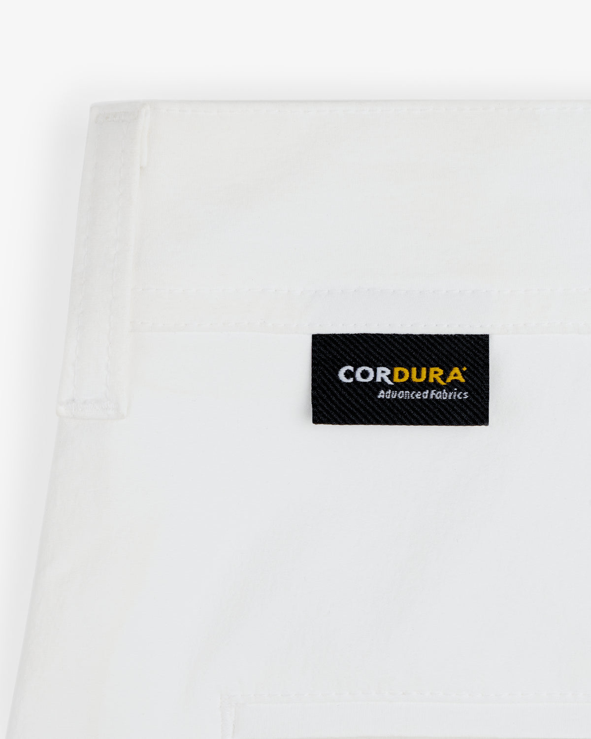 Close-up of ALD Golf Cordura Double Pleated Pant's white fabric with a black CORDURA Advanced Fabrics label stitched on.