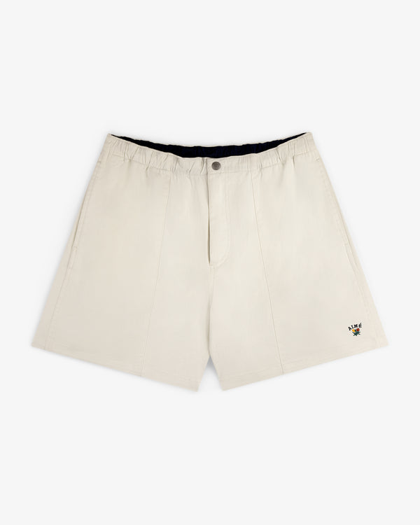 Crest Casual Short in beige with side pockets and a small floral embroidery near the hem, shown on white background.