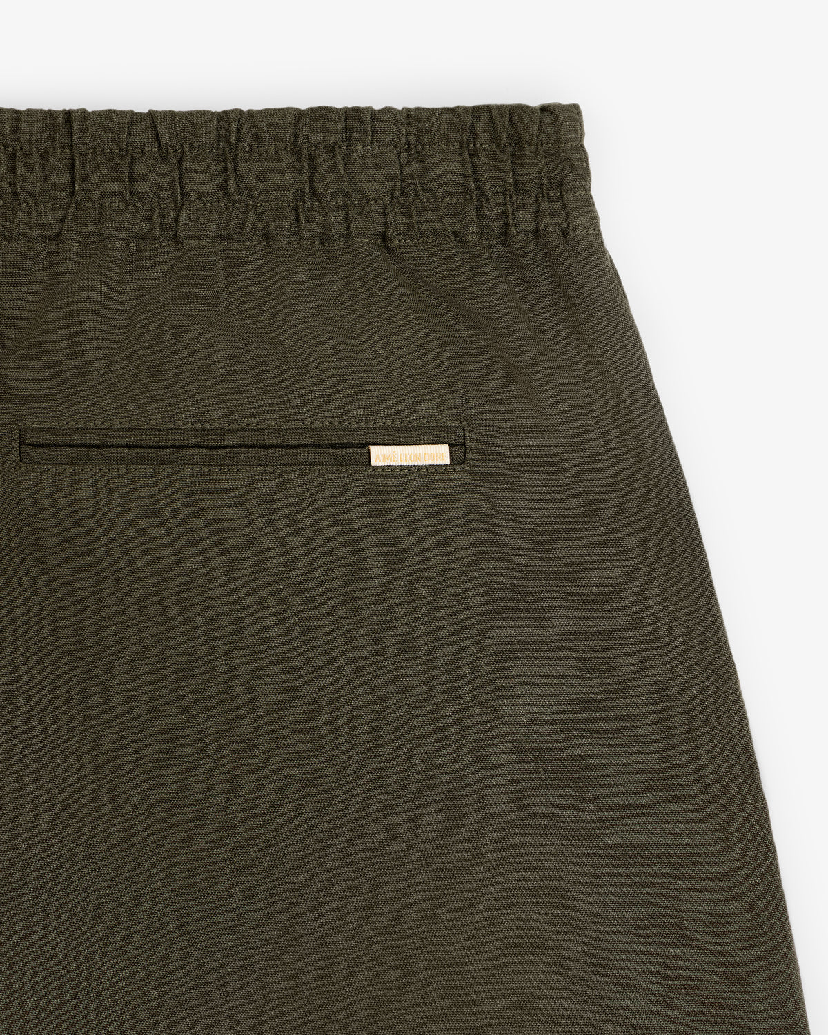 Close-up of Linen Leisure Short in olive green with elastic waistband and back pocket featuring a metallic brand tag.