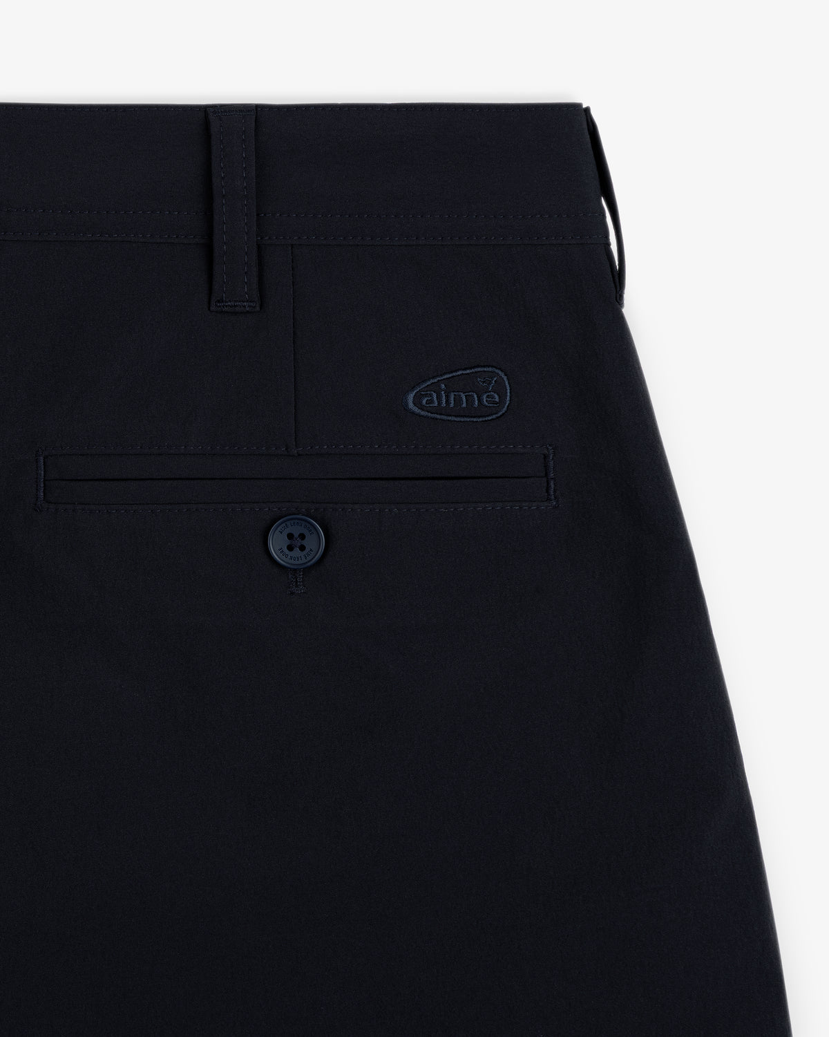 Close-up of ALD Golf Cordura Double Pleated Short's navy pocket with button and small aime logo on white background.