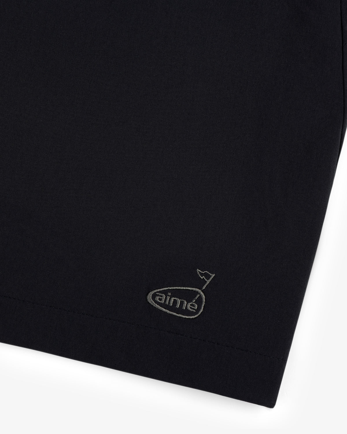 Close-up of the ALD Golf Performance Short in black with a small aimé logo and tiny flag embroidered near the hem.