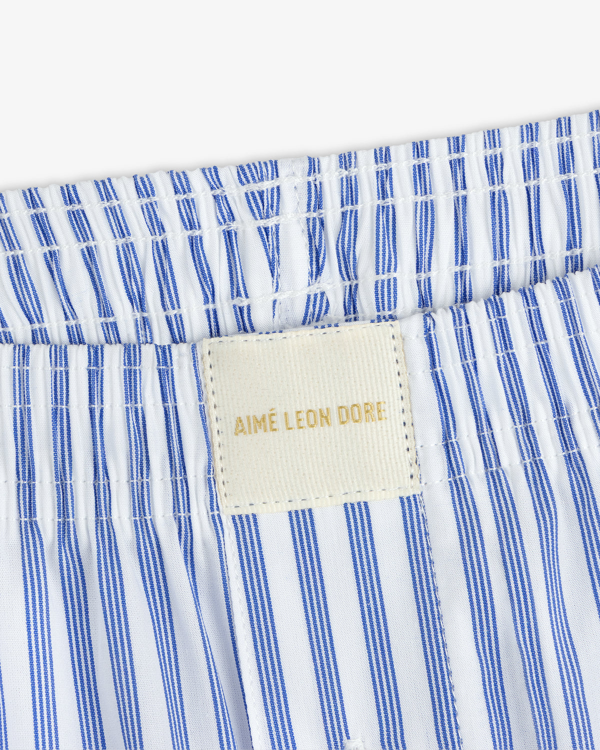 Close-up of Striped Boxer Short's blue-and-white waistband with a cream AIMÉ LEON DORE label stitched on.