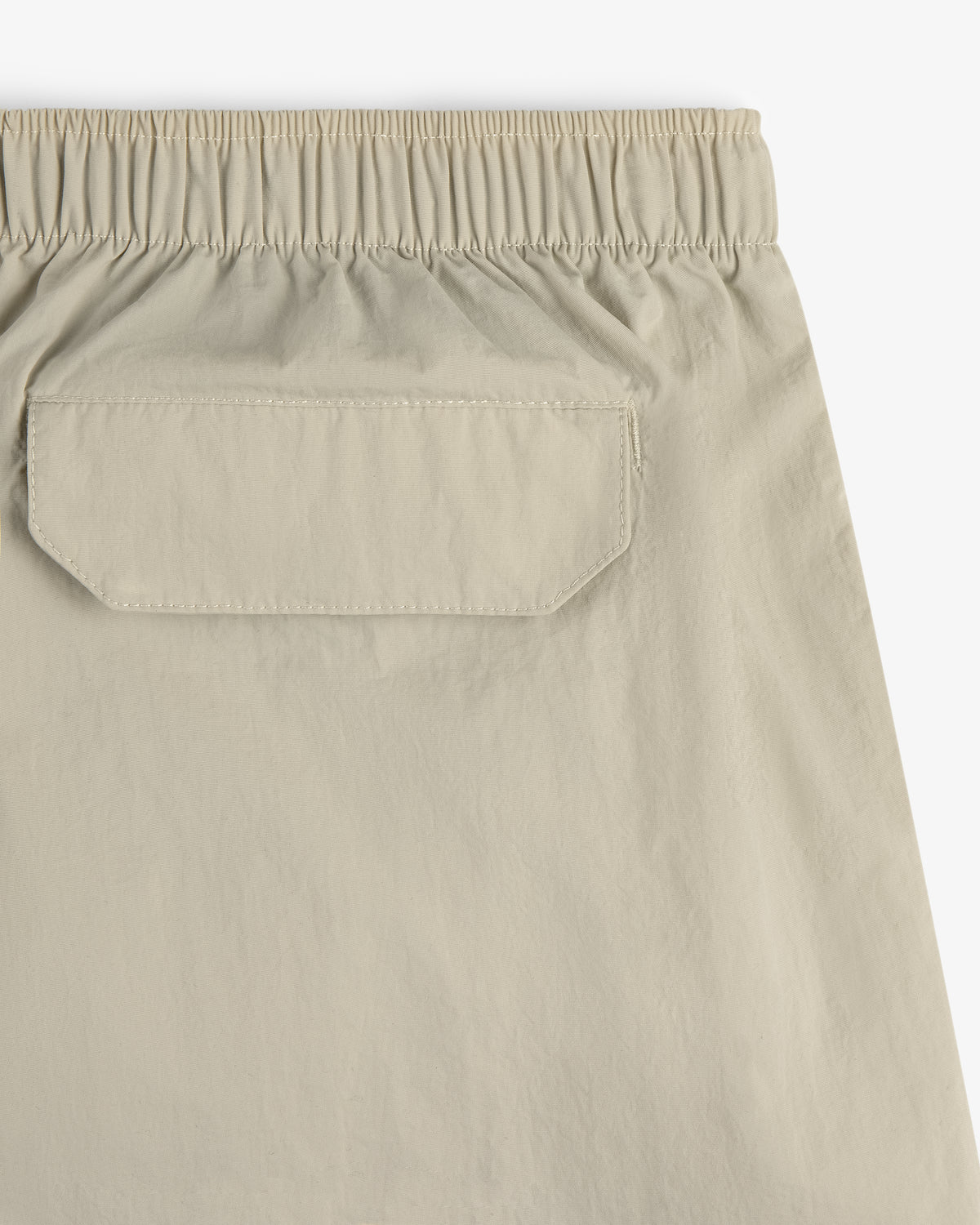Close-up of the back of Core Nylon Short in beige, featuring an elastic waistband and a flap pocket.