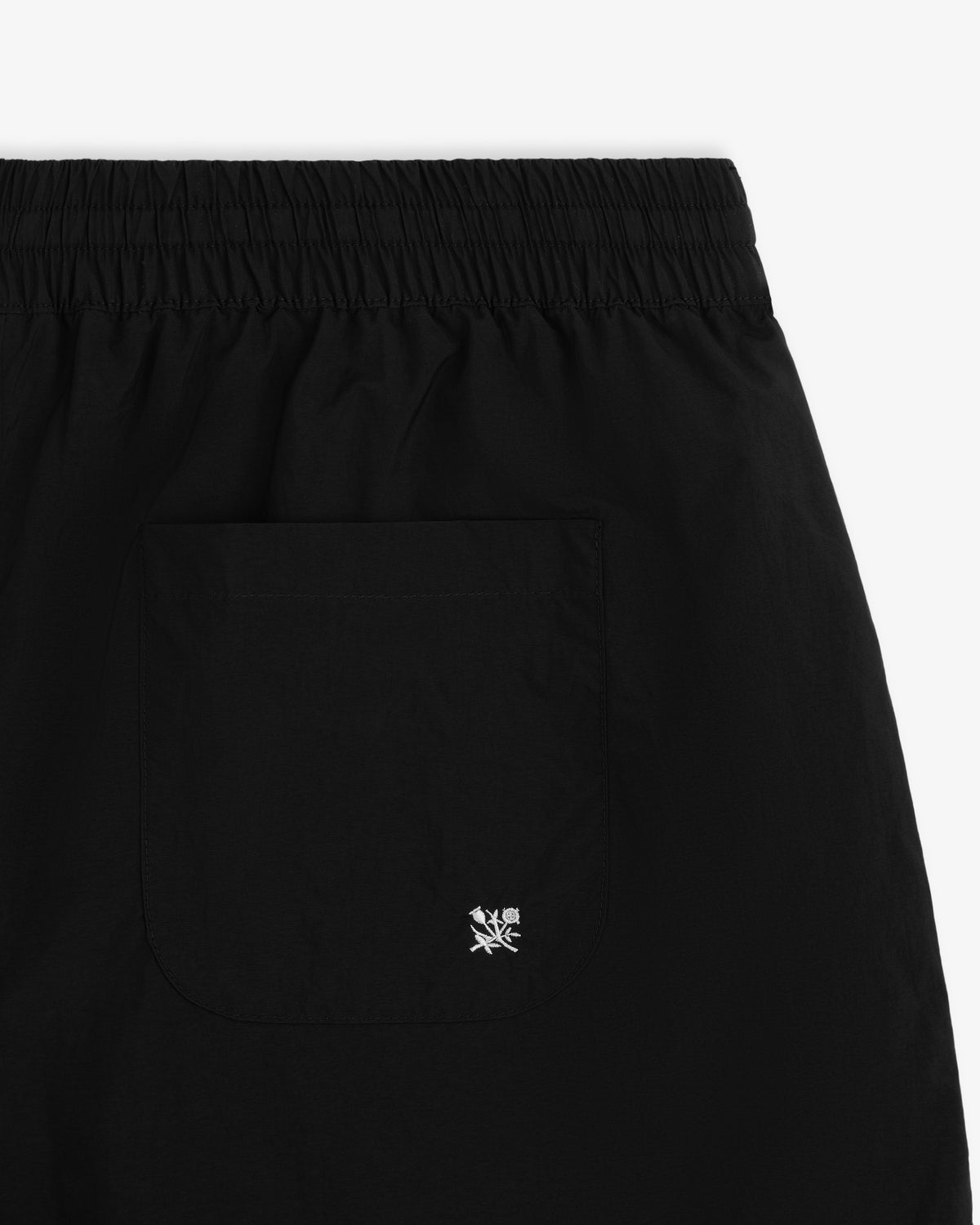 Close-up of the Long Nylon Track Short in black with an elastic waistband, back pocket, and small white logo embroidery.