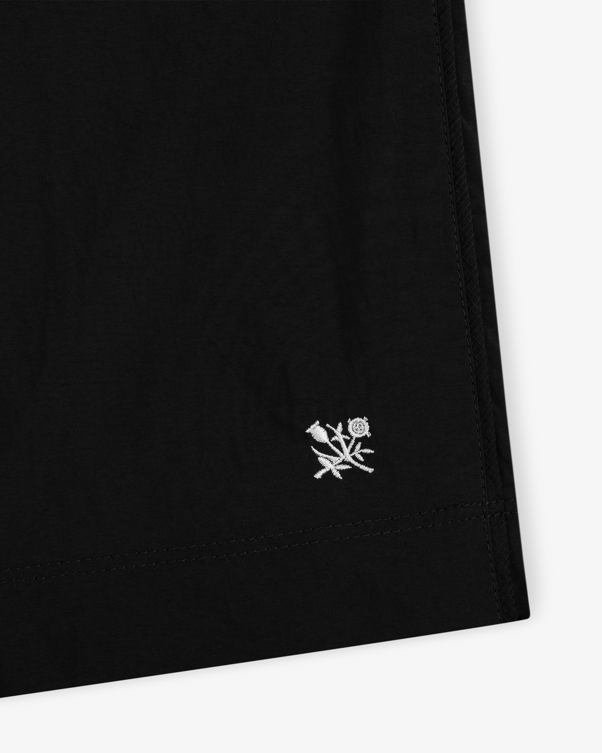 Close-up of Long Nylon Track Short in black with small white embroidered flower and leaf near the hem.