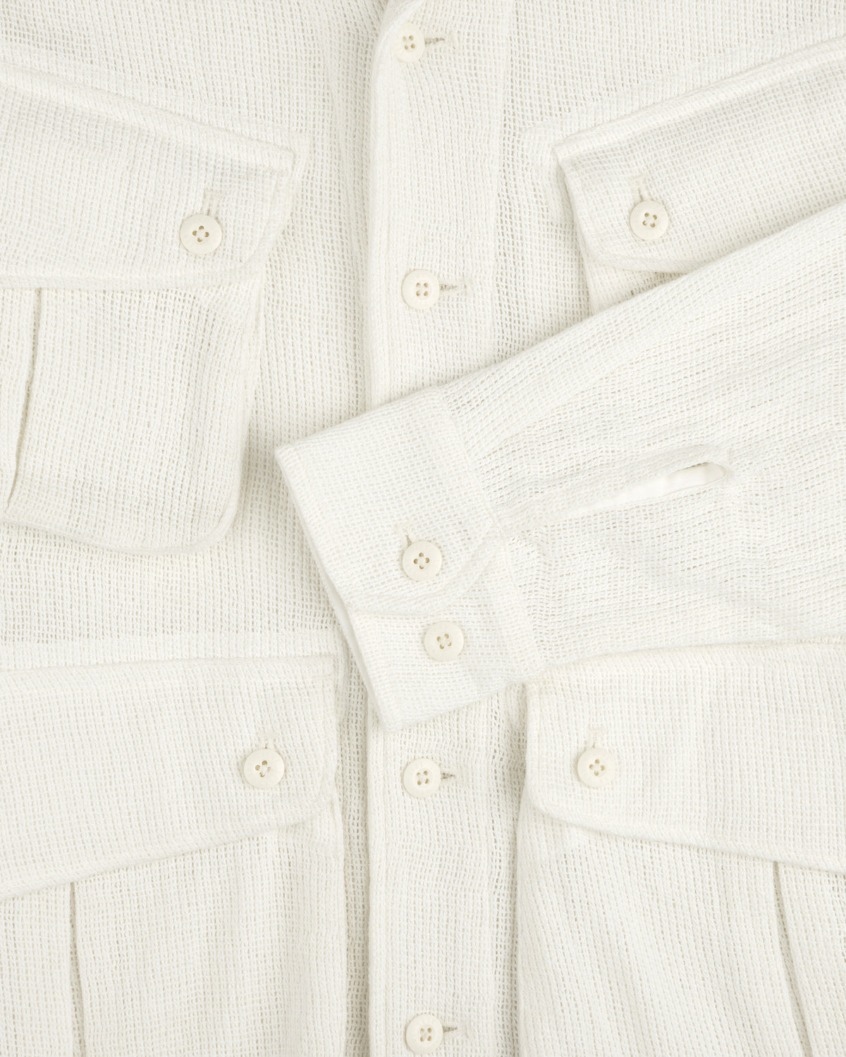 Close-up of the Mesh Jungle Shirt, cream-colored with textured fabric, buttons, flap pockets, and one sleeve across the front.