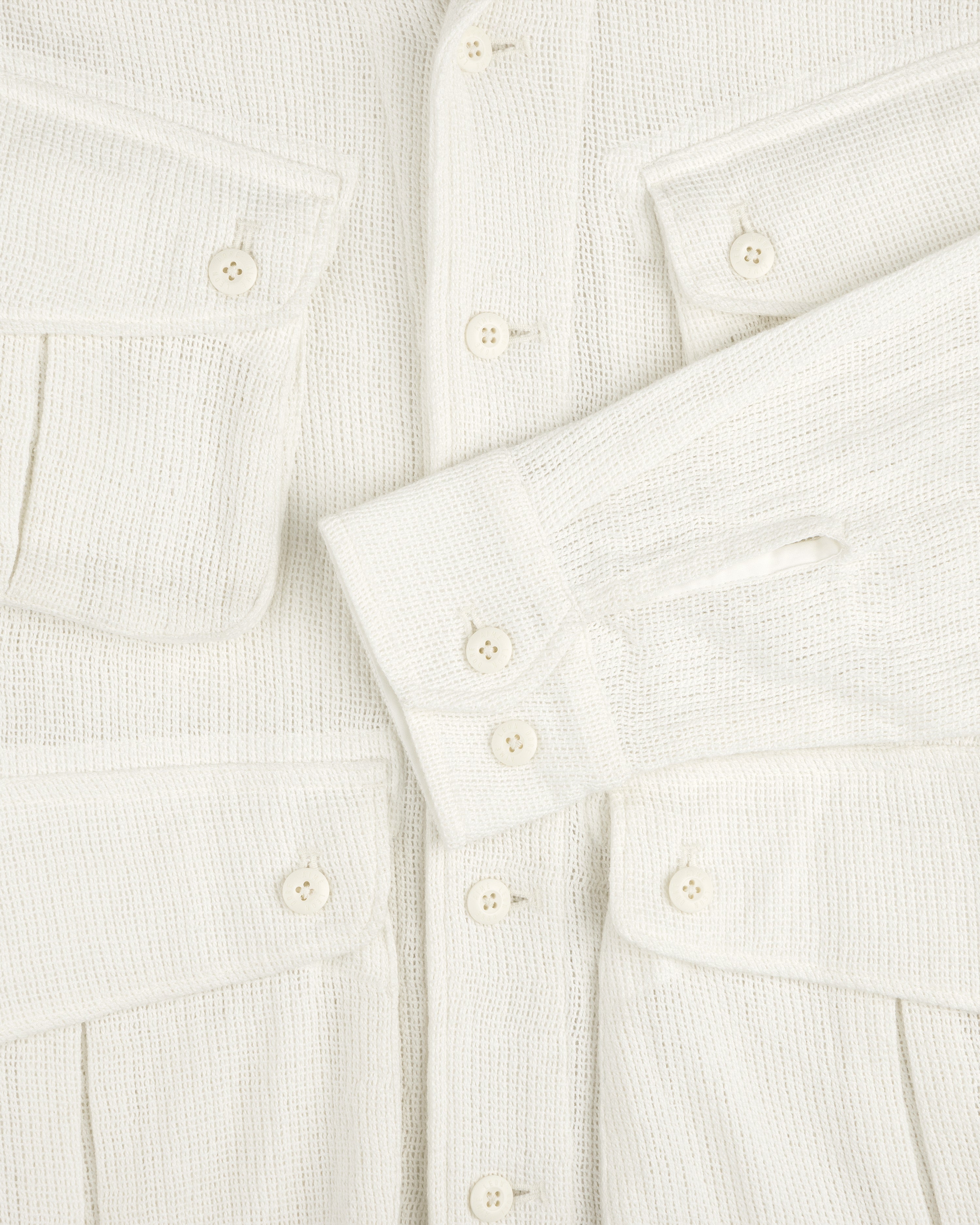 Close-up of the Mesh Jungle Shirt, cream-colored with textured fabric, buttons, flap pockets, and one sleeve across the front.