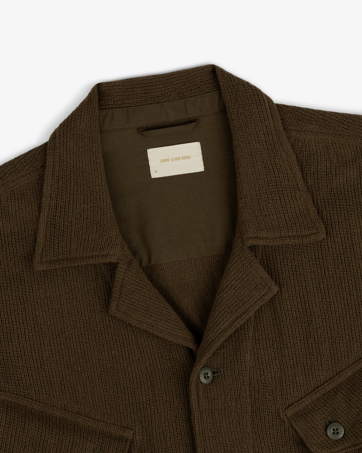 Close-up of the Mesh Jungle Shirt—a brown, textured button-up with collar and chest pocket, laid flat on white.