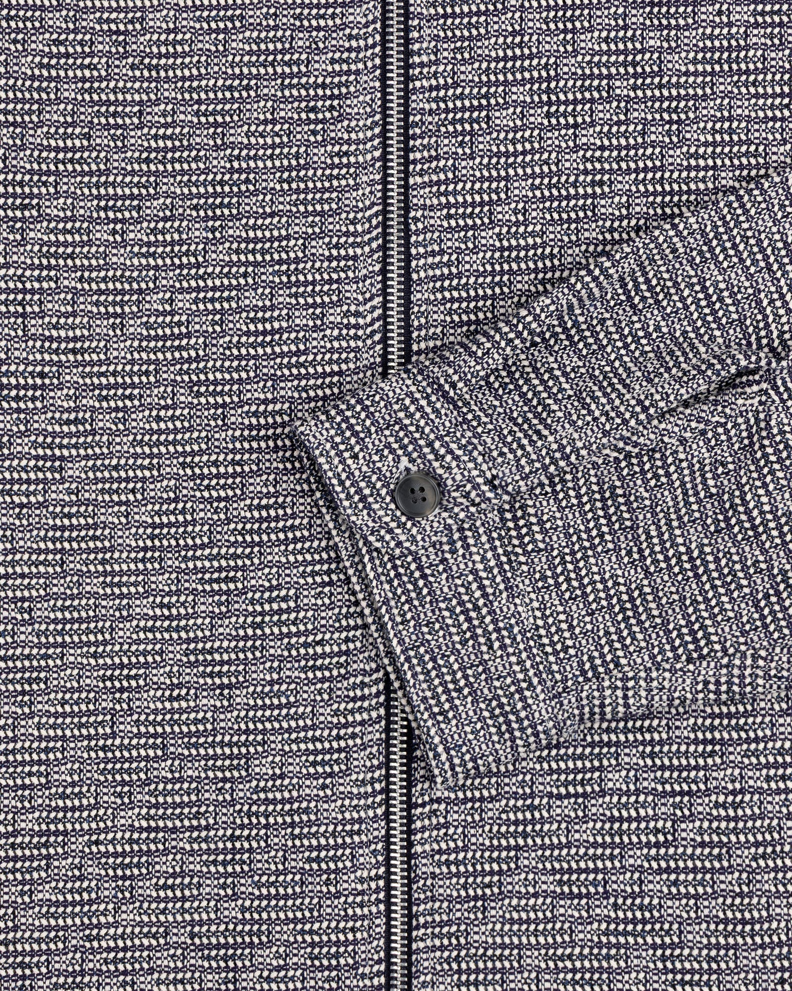 Close-up of the Textured Zip Shirt: gray and black patterned fabric with a sleeve and black button.