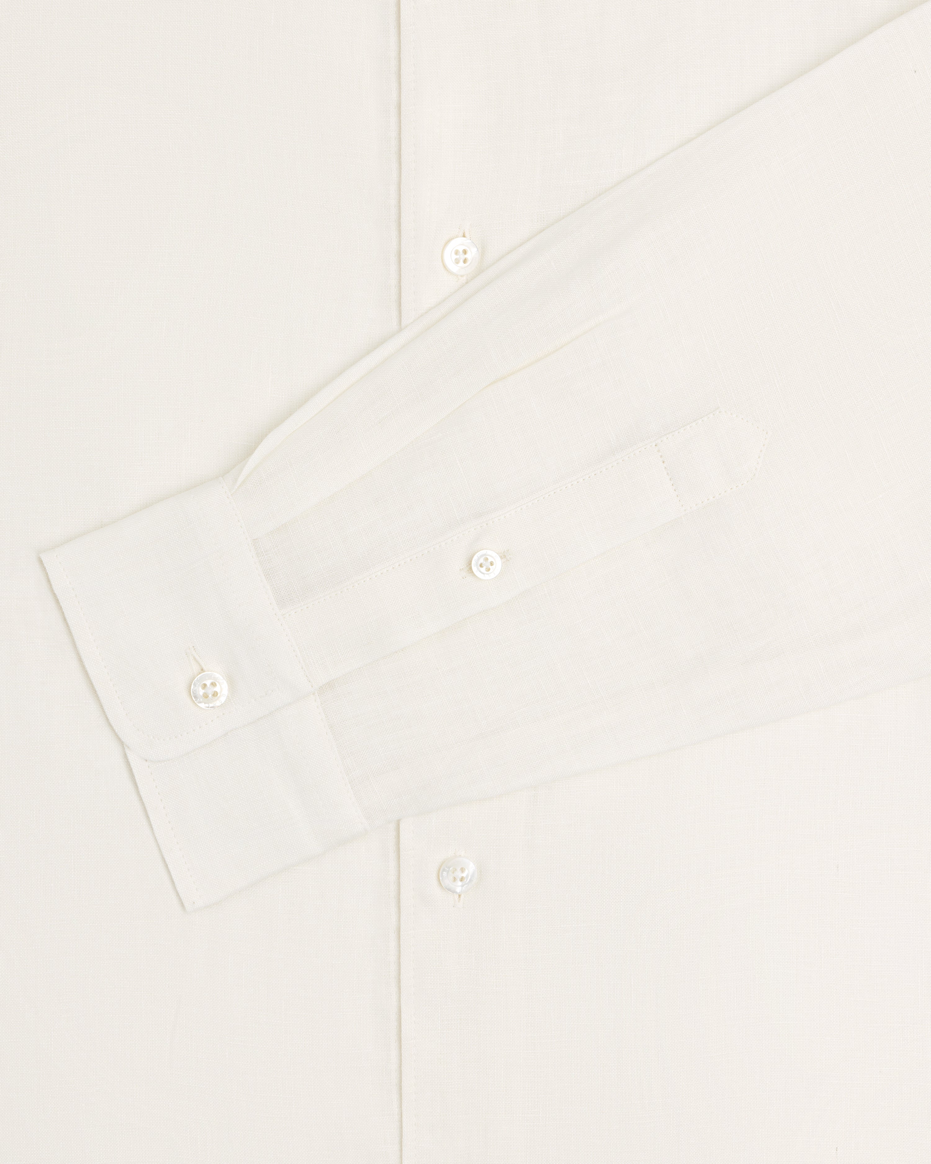 A close-up of the Long-Sleeve Linen Shirt displays its sleeve, cuff, and buttons against a light background.