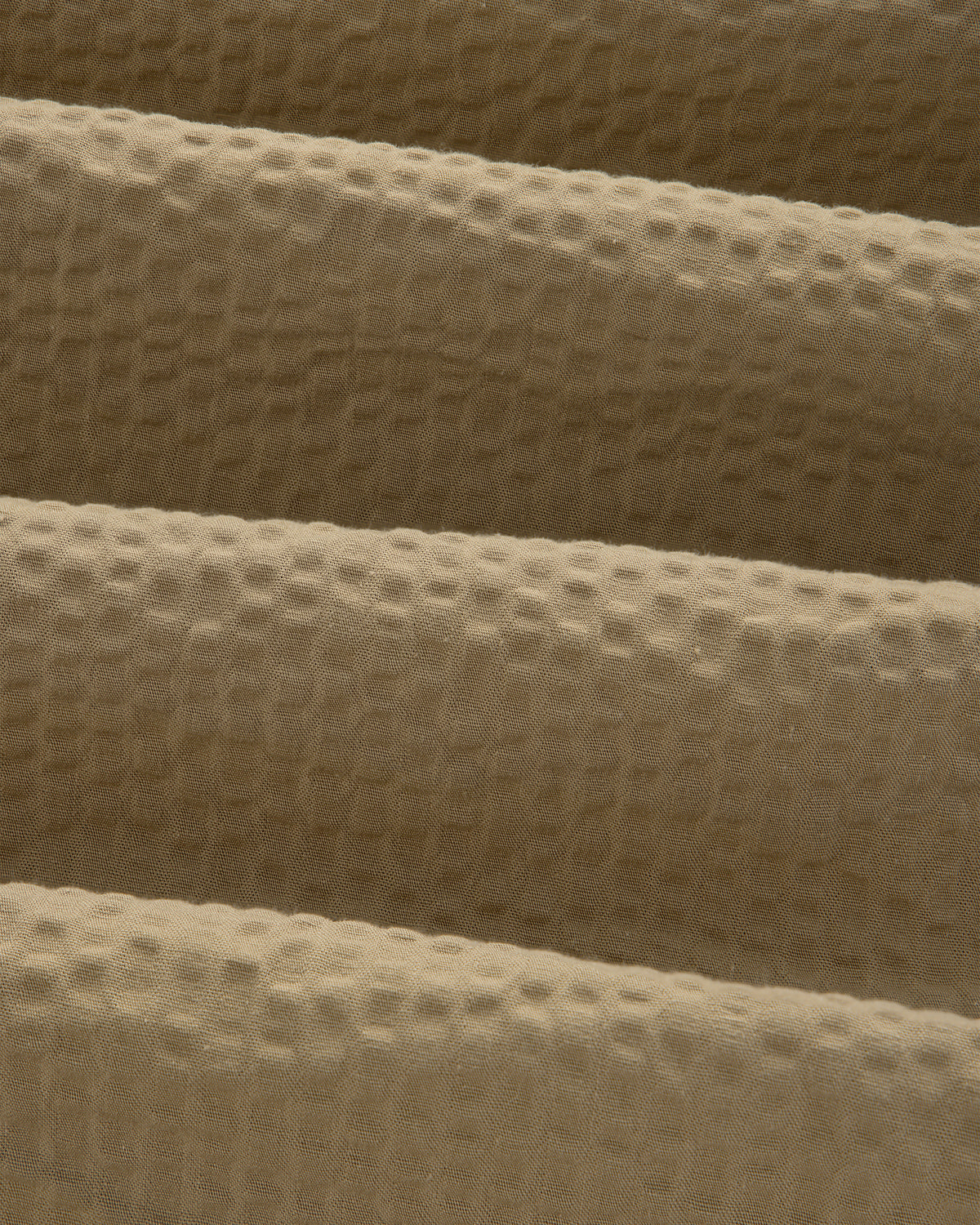 Close-up of beige, waffle-textured fabric with gentle folds on a Short-Sleeve Seersucker Shirt.