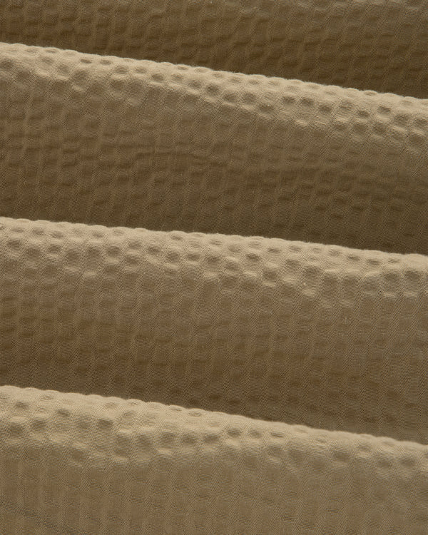 Close-up of beige, waffle-textured fabric with gentle folds on a Short-Sleeve Seersucker Shirt.