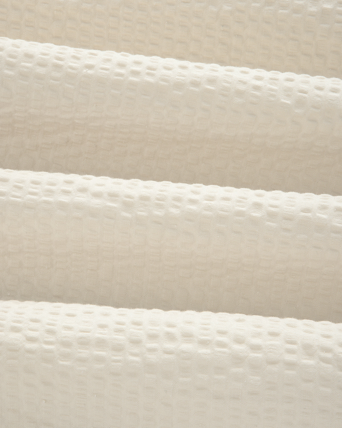 Close-up of the Short-Sleeve Seersucker Shirt's cream, textured fabric with a raised grid pattern and soft folds.