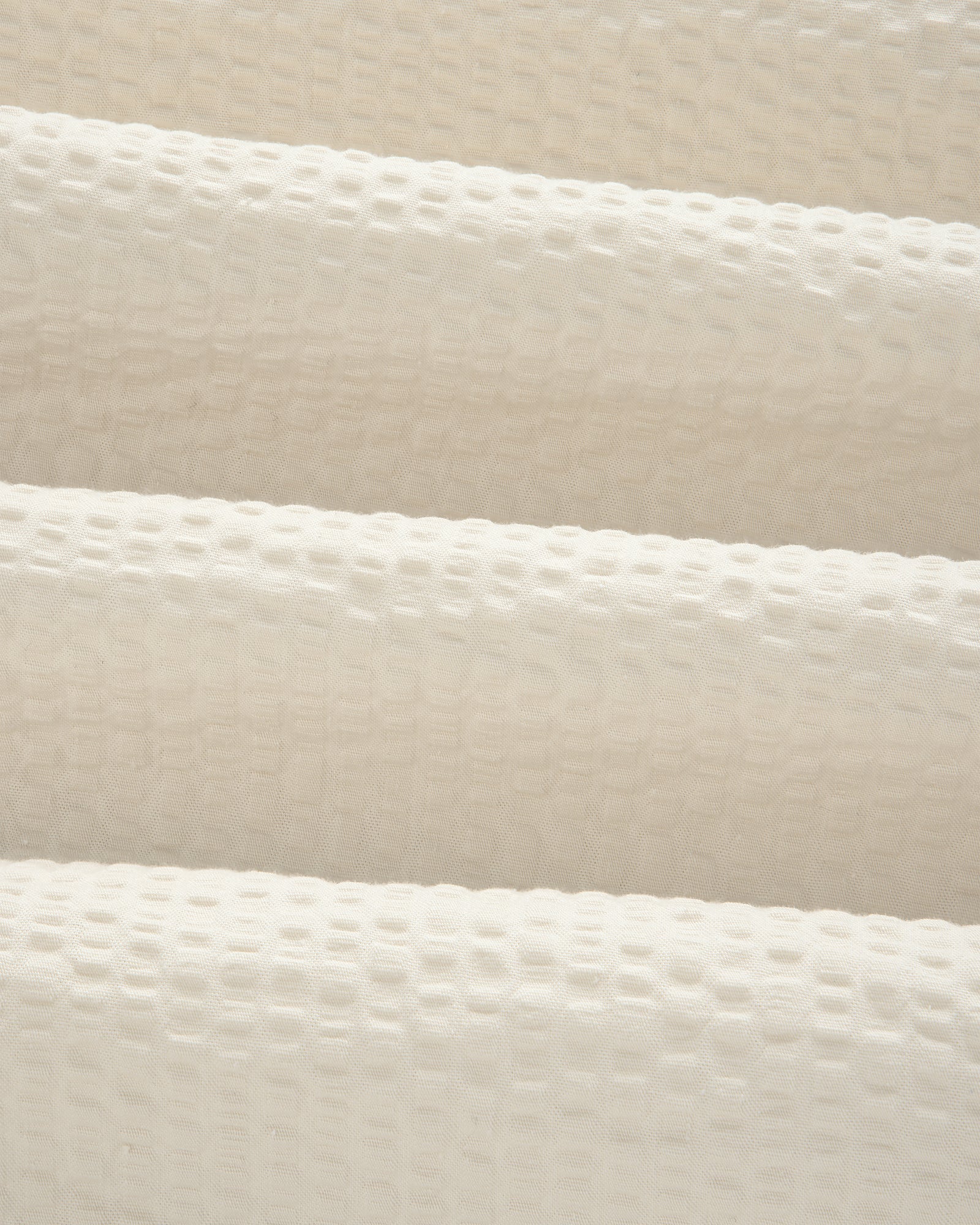 Close-up of the Short-Sleeve Seersucker Shirt's cream, textured fabric with a raised grid pattern and soft folds.
