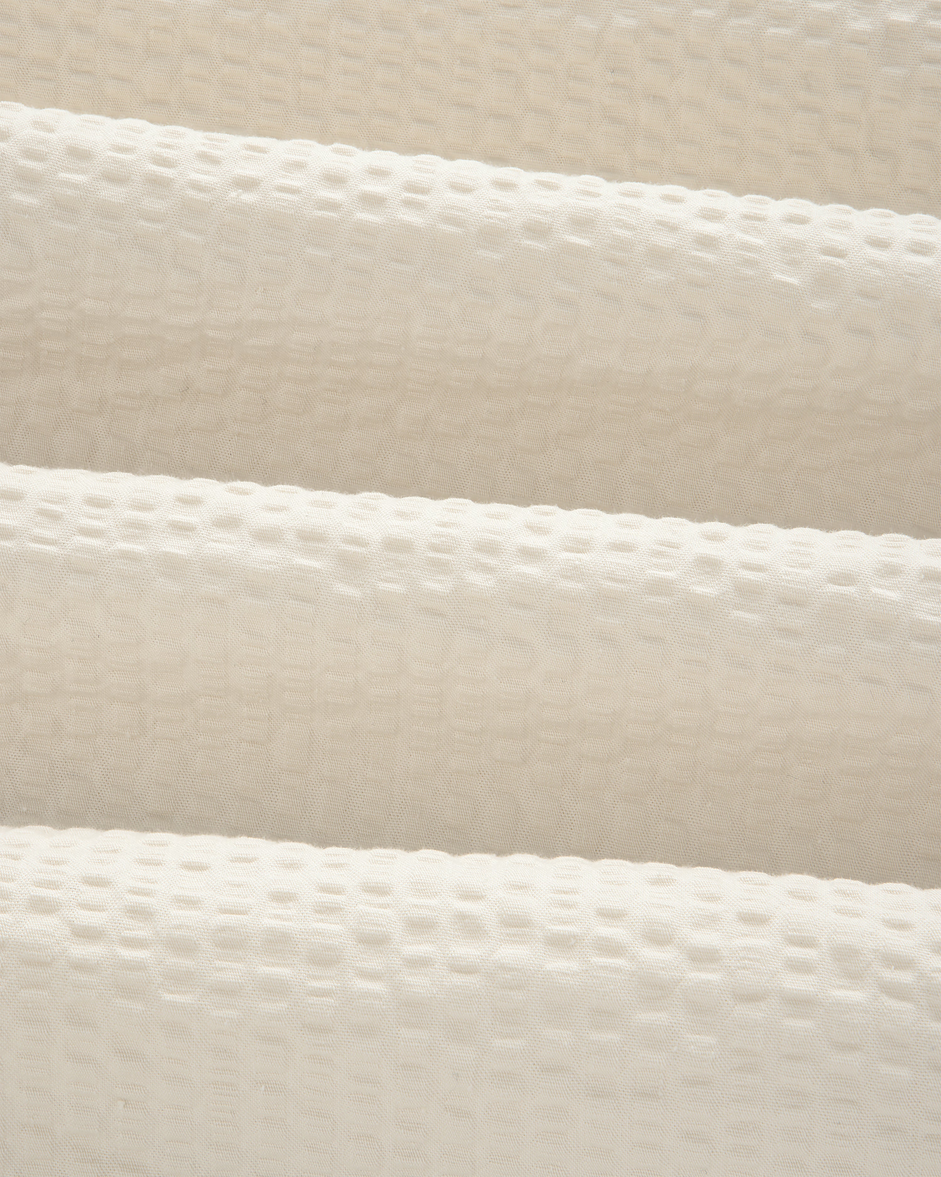 Close-up of the Short-Sleeve Seersucker Shirt's cream, textured fabric with a raised grid pattern and soft folds.