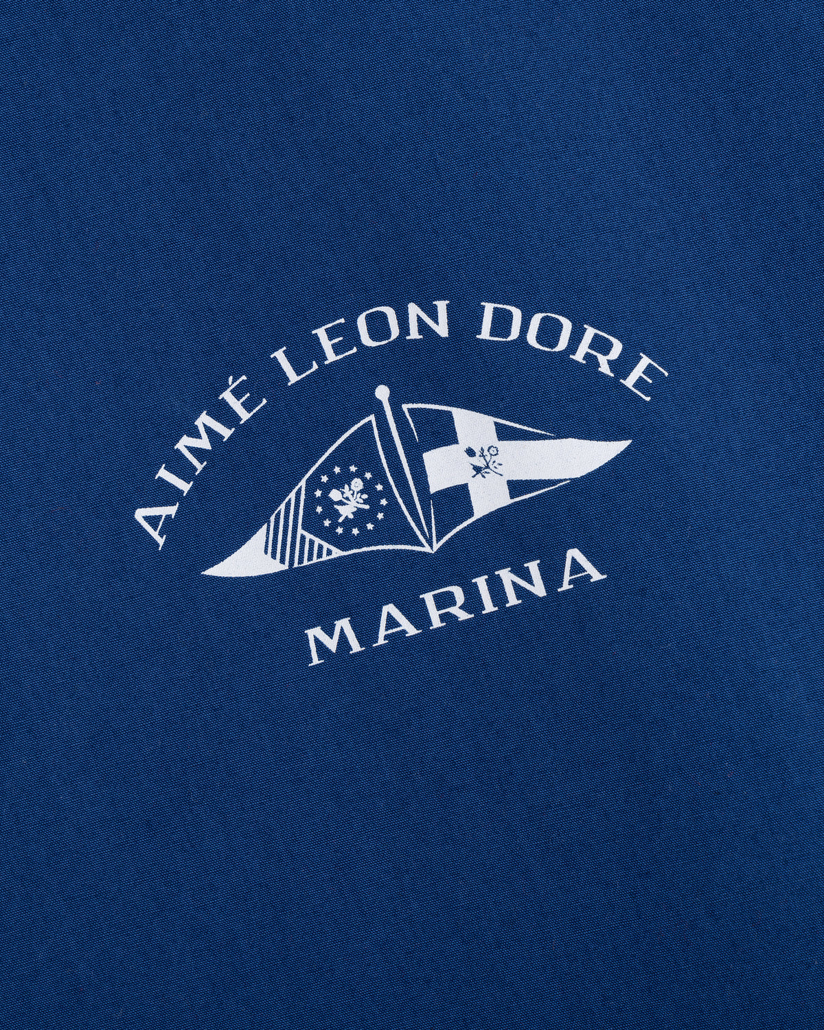 Blue fabric Marina Jacket featuring AIMÉ LEON DORE MARINA text and two white nautical flags printed below.