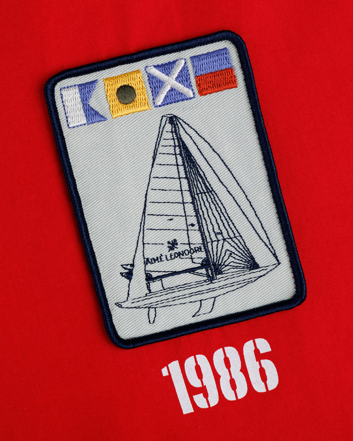 The Marina Jacket features an embroidered sailboat patch with nautical flags and SAINT LEONORE on red, "1986" below.