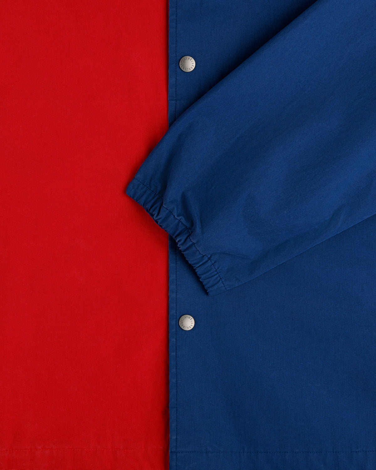 Close-up of the Marina Jacket with a red body, blue sleeve, silver snap buttons, and an elastic cuff.