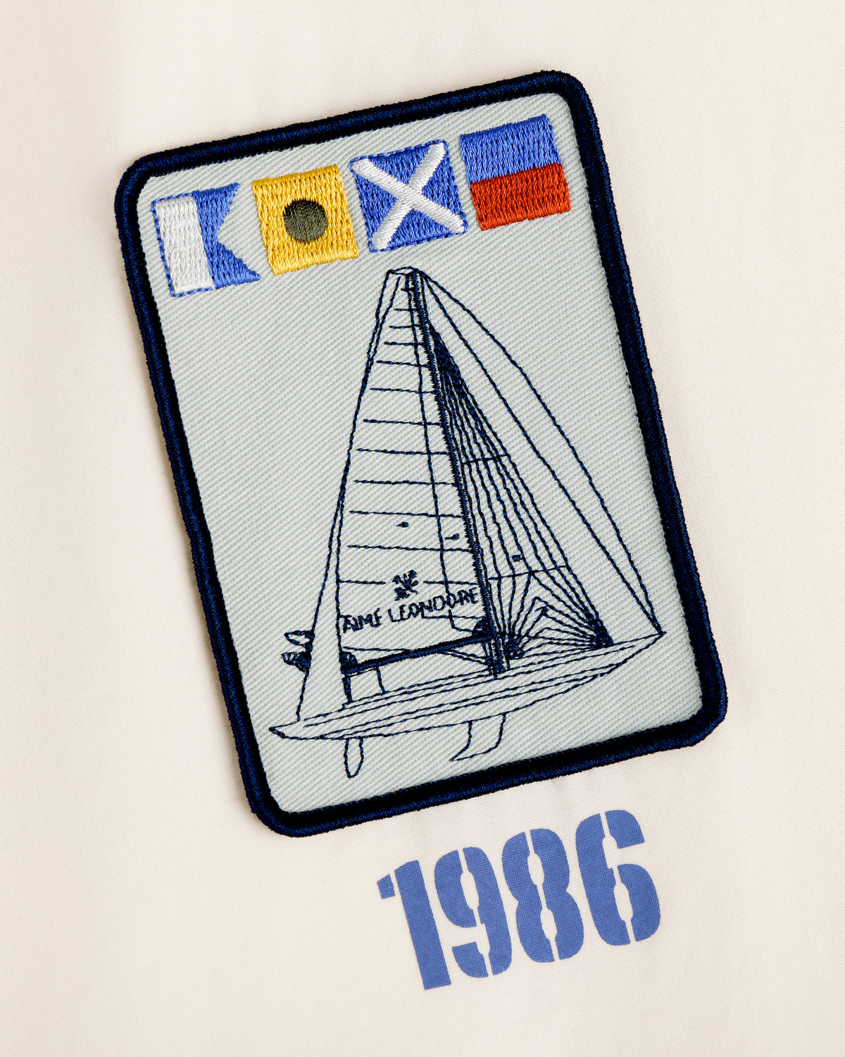 Marina Jacket with embroidered sailboat, flag symbols, and “1986 Fame Leonardine” on a light background.