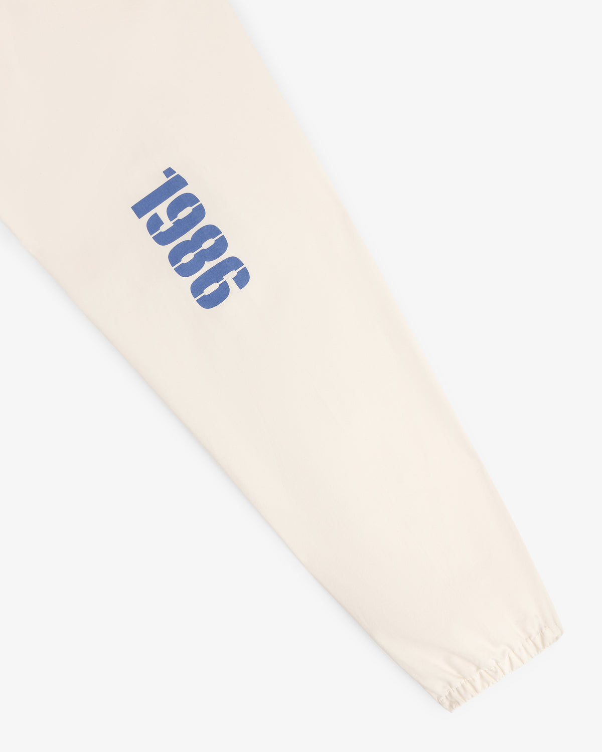 The Marina Jacket features a beige sleeve with vertical blue 1986 text and an elastic cuff at the wrist.